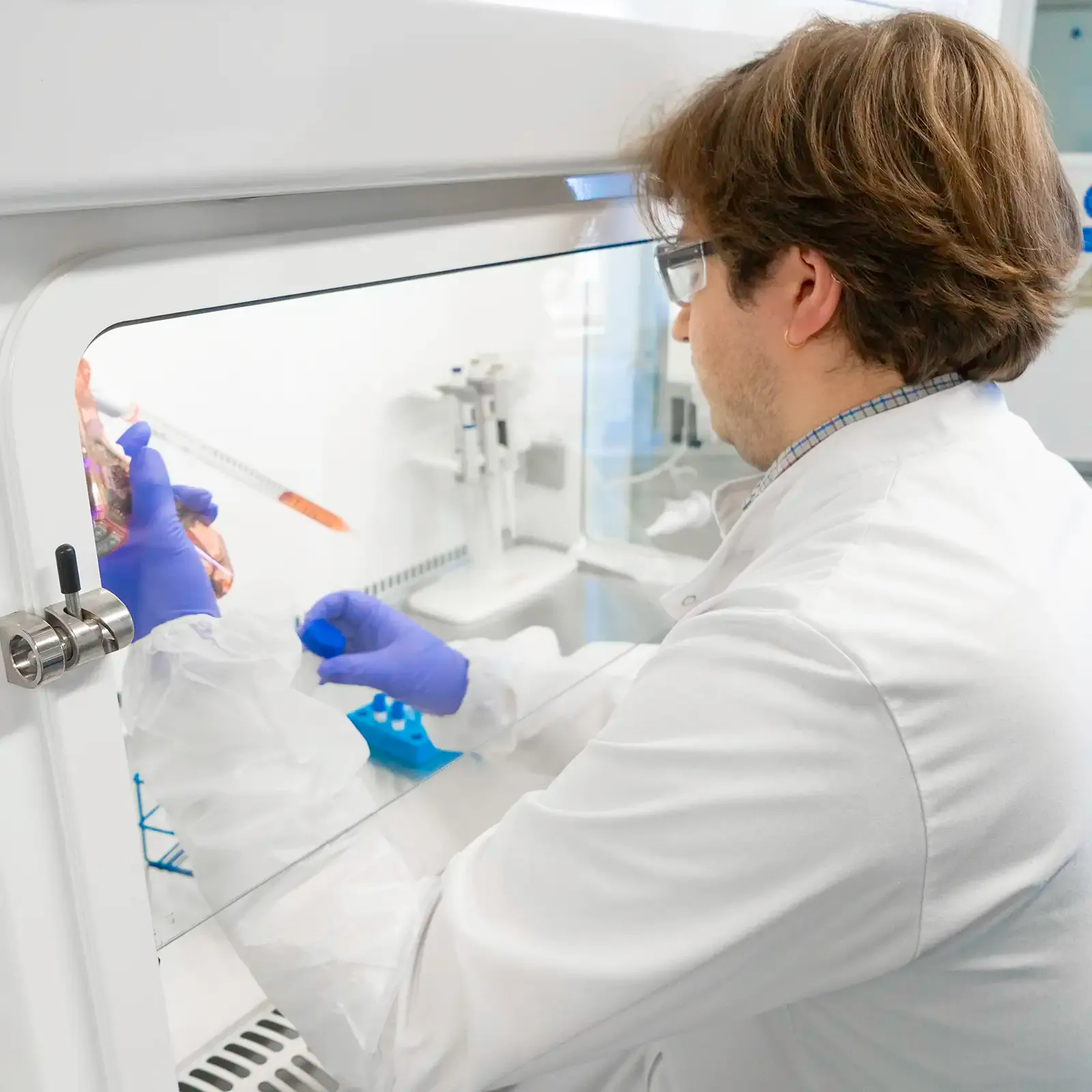 Laboratory scientist pipetting with arms inside fume cupboard